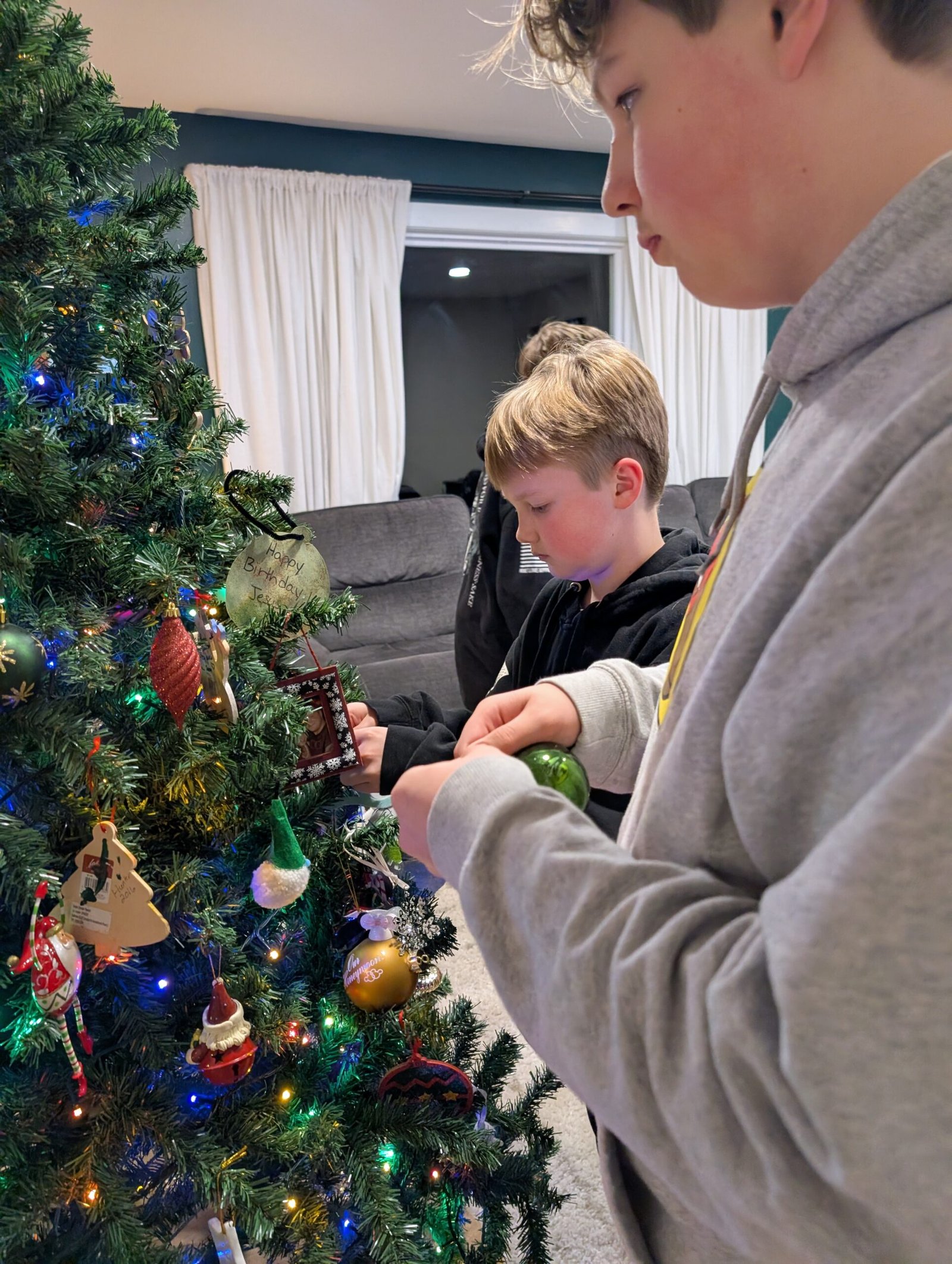 Unboxing Memories: How Our Christmas Tree Became a Timeline of Grace, Growth, and God's Faithfulness Hunter and Sawyer carefully placing ornaments on the Christmas tree, sharing a brotherly moment.