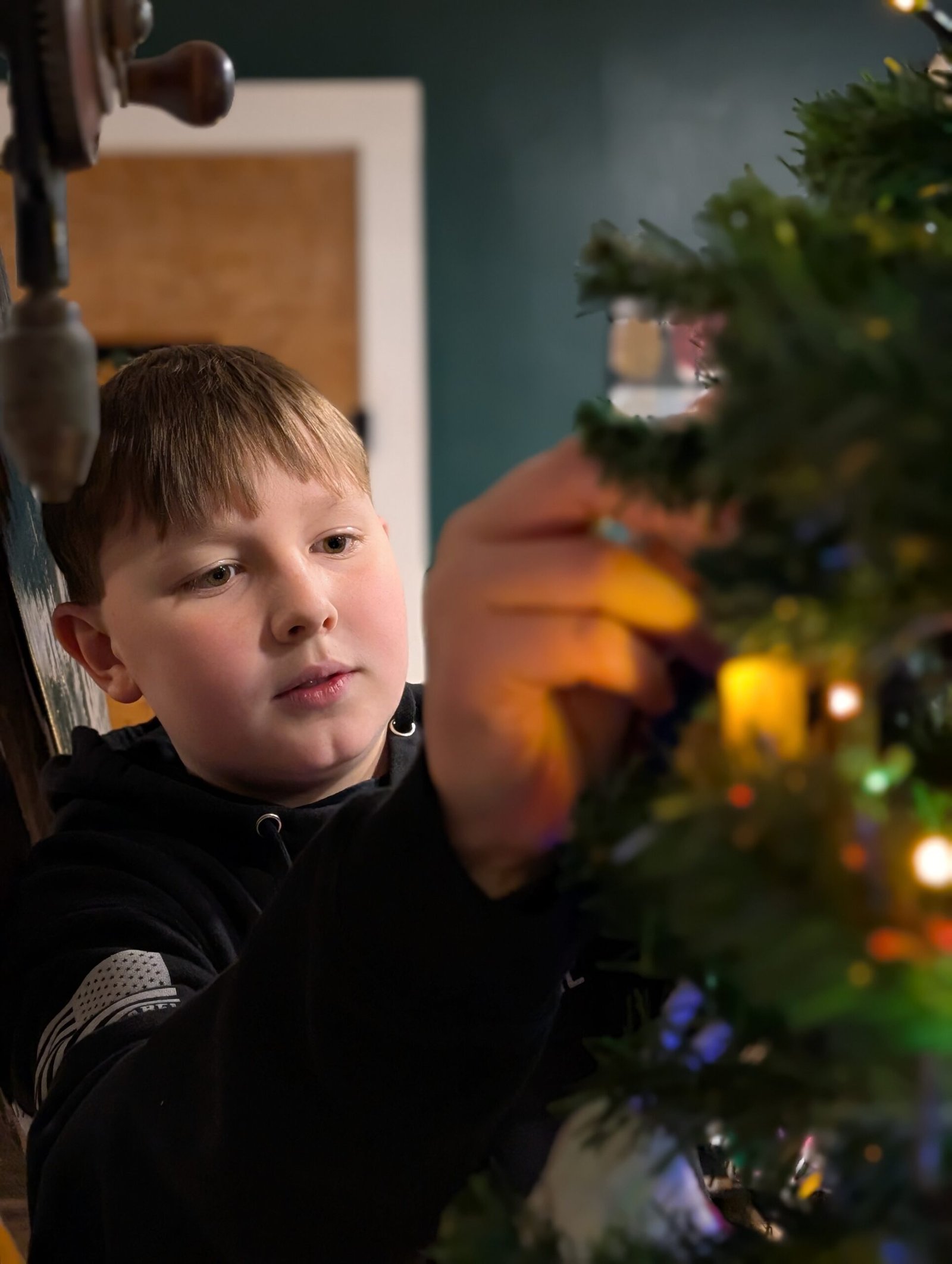 Unboxing Memories: How Our Christmas Tree Became a Timeline of Grace, Growth, and God's Faithfulness Nathan carefully hanging a cherished ornament on the Christmas tree, lost in thought.